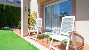 A patio with white chairs and a small table, a green lawn, and a building with large windows and a door. - Holiday Home 'Isla Bonita' with Sea Views, Wi-Fi and Air Conditioning (Mont-roig del Camp)