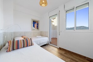 Une chambre à coucher avec un lit, une fenêtre donnant sur un beau paysage, une porte menant à un balcon et un luminaire fixé au mur.