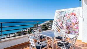 Un balcon avec une table et des chaises, donnant sur une plage et la mer.