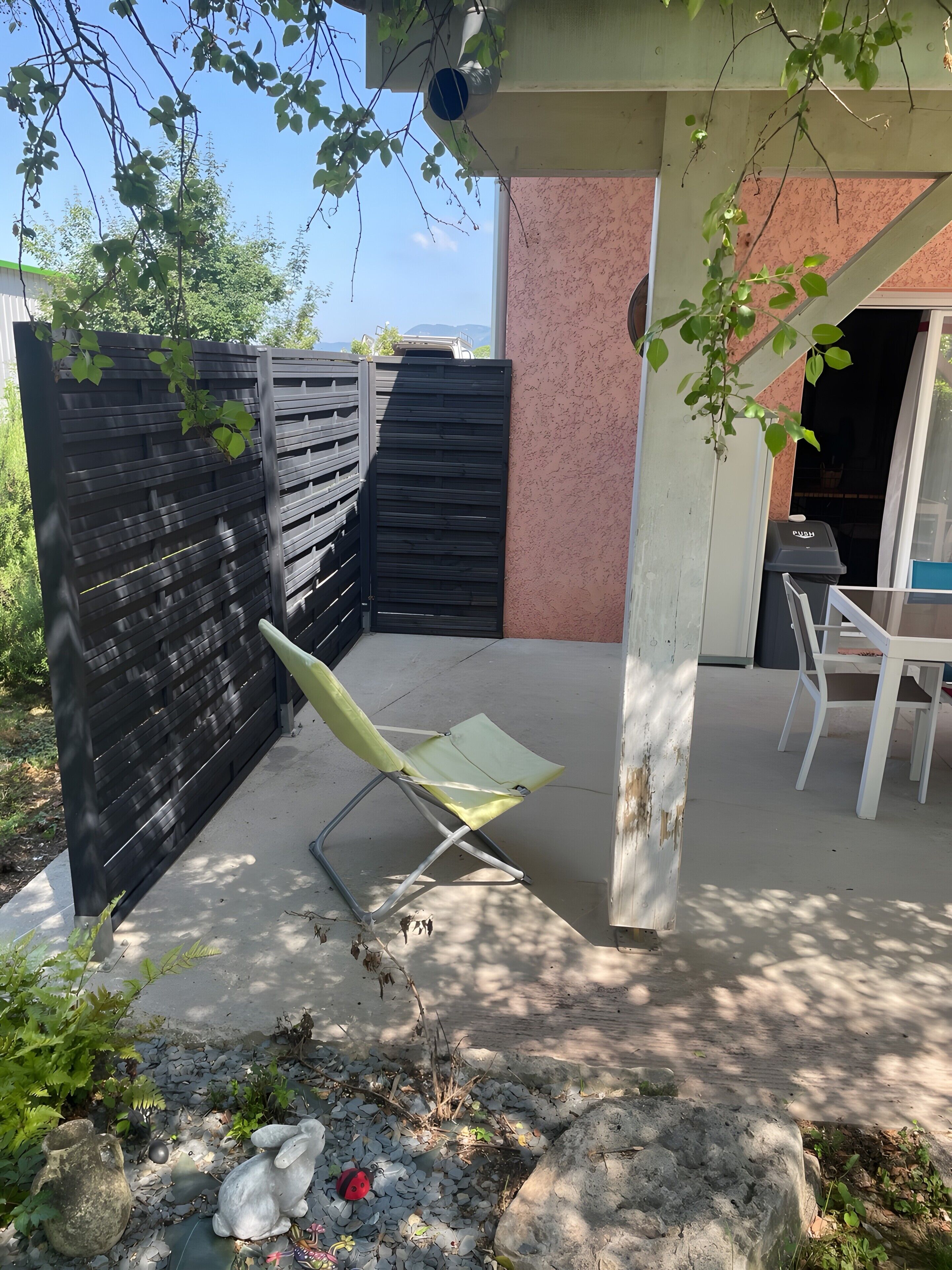 A patio area with a metal chair, a concrete floor, a black fence, and a building with pink walls.