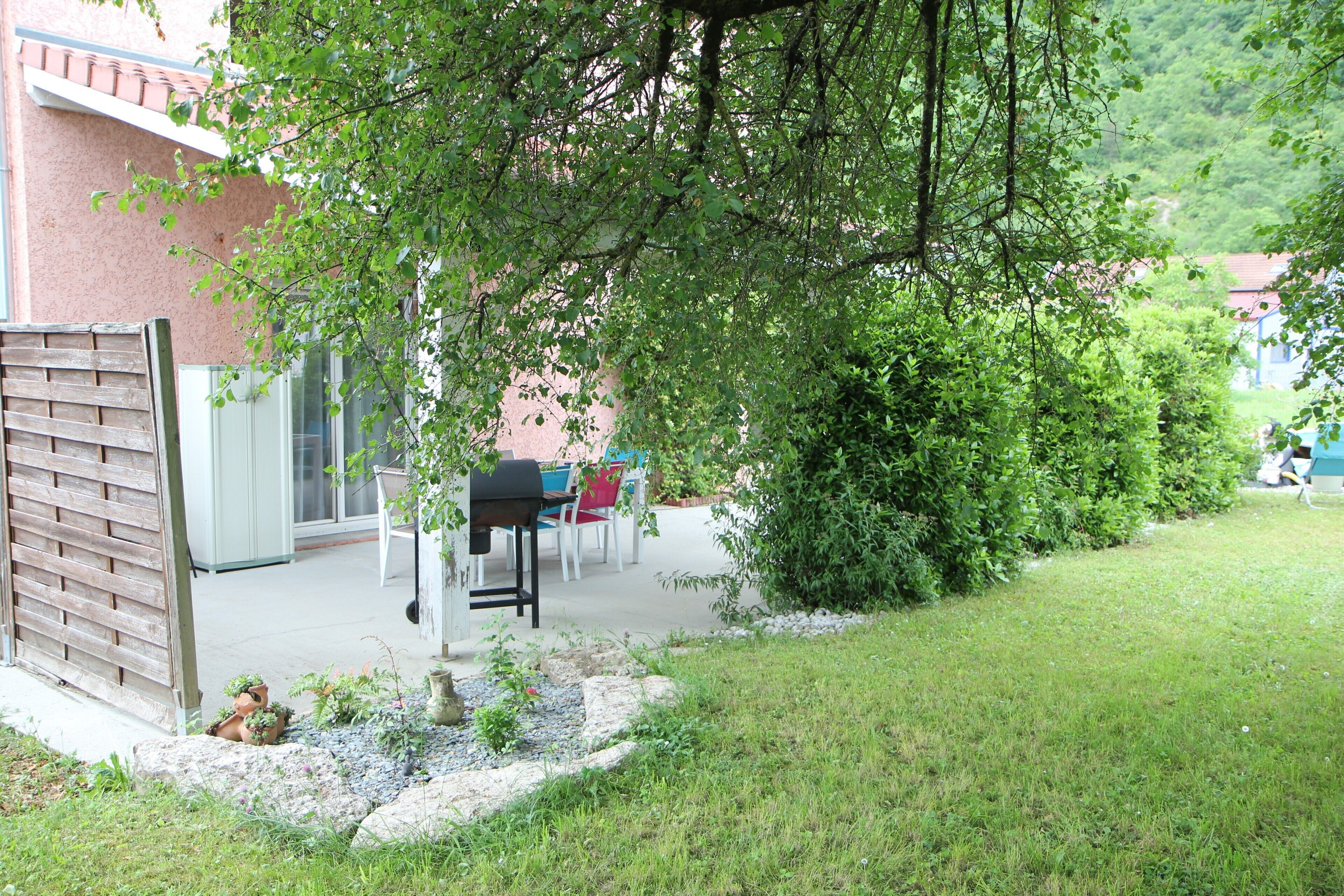 Un espace patio aménagé avec un barbecue, des sièges d’extérieur et un jardin agrémenté de rochers et de plantes.