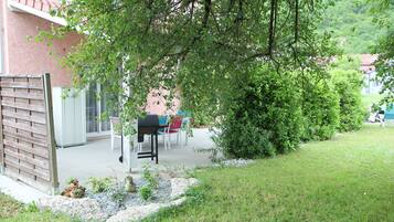 Un espace patio aménagé avec un barbecue, des sièges d’extérieur et un jardin agrémenté de rochers et de plantes.