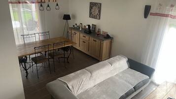 A dining area with a wooden table and chairs, a sofa, a cabinet with decorative items, and a clock on the wall.