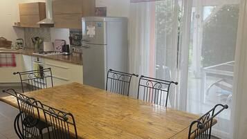 A kitchen with a wooden table and chairs, a refrigerator, and a window with curtains.