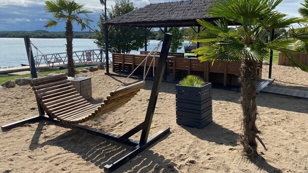 Una zona sulla spiaggia con un'amaca, una struttura a tetto di paglia e palme.