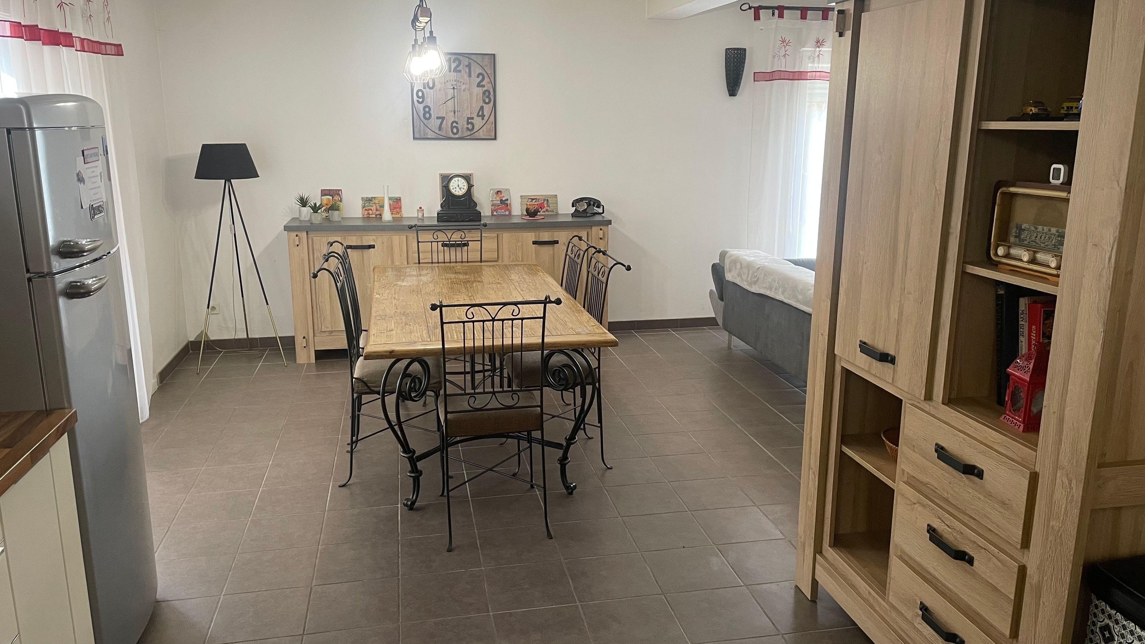 Une cuisine de taille réduite comprenant une table à manger, des chaises, un réfrigérateur, une horloge et un placard.