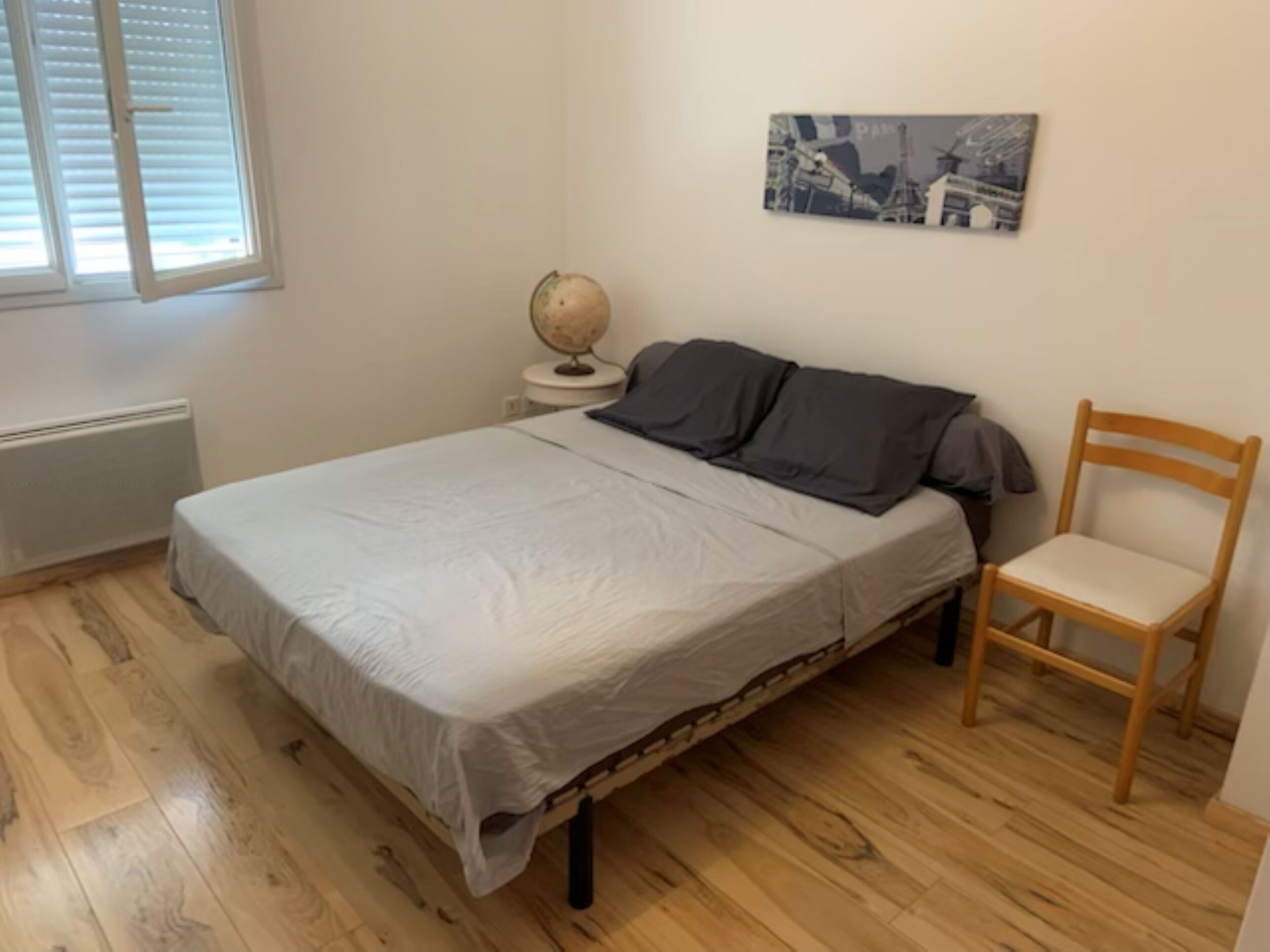 Een slaapkamer met een bed, een wereldbol op een nachtkastje, een stoel en een aan de muur hangend schilderij.