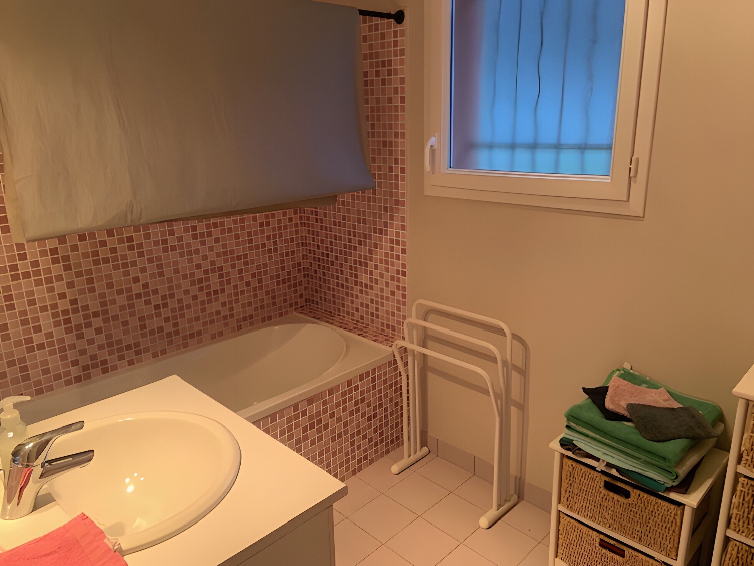 Ein Badezimmer mit einer Badewanne, einem Waschbecken, einem Fenster und einem Handtuchhalter.