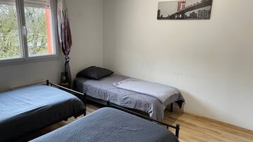 Een studentenkamer met twee eenpersoonsbedden, een radiator, een raam met gordijnen en een stadsgezichtposter aan de muur.