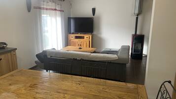 A living room with a sofa, a television, a wooden cabinet, and a dining table.