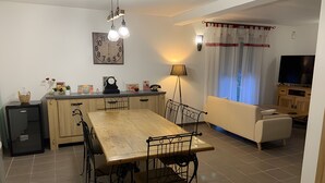 Una cucina moderna con tavolo e sedie in legno, zona pranzo con divano, TV e orologio appeso al muro.