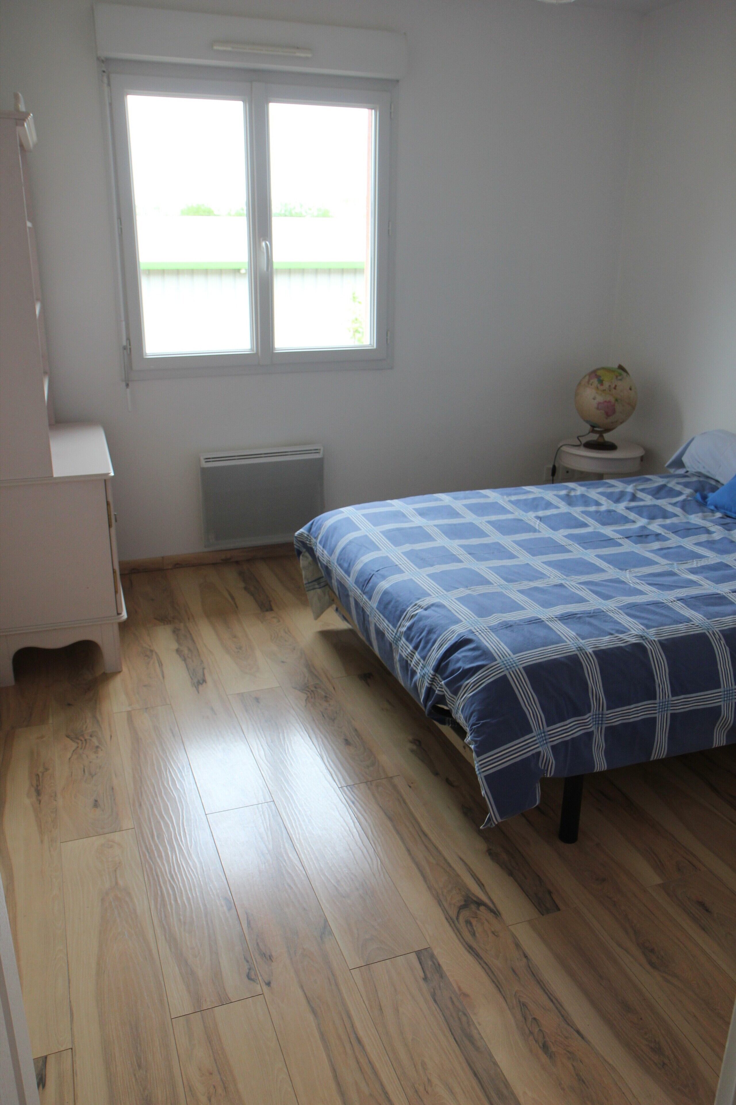 A bedroom with a bed, a dresser, a radiator, and a window with a view.