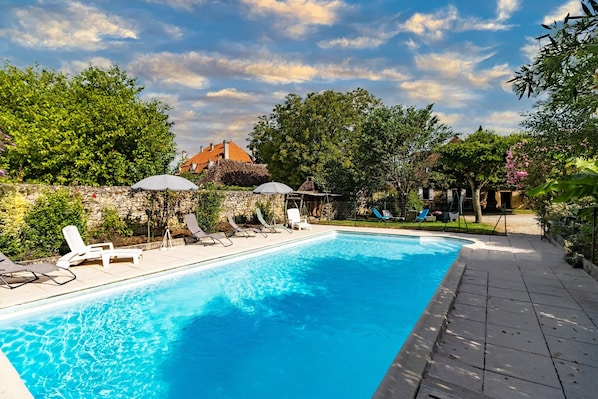 A rectangular swimming pool with clear blue water, surrounded by lounge chairs and umbrellas.