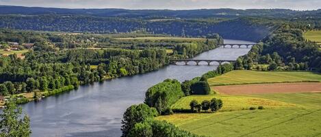 A river with a bridge, green fields, and distant hills.