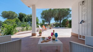 An outdoor patio with wicker chairs, a table with food and drinks, and a view of trees and a road. - Villa 'Nonna Anna' with Pool, Private Terrace, Wi-Fi, Wood Oven, and Barbecue (Siracusa)