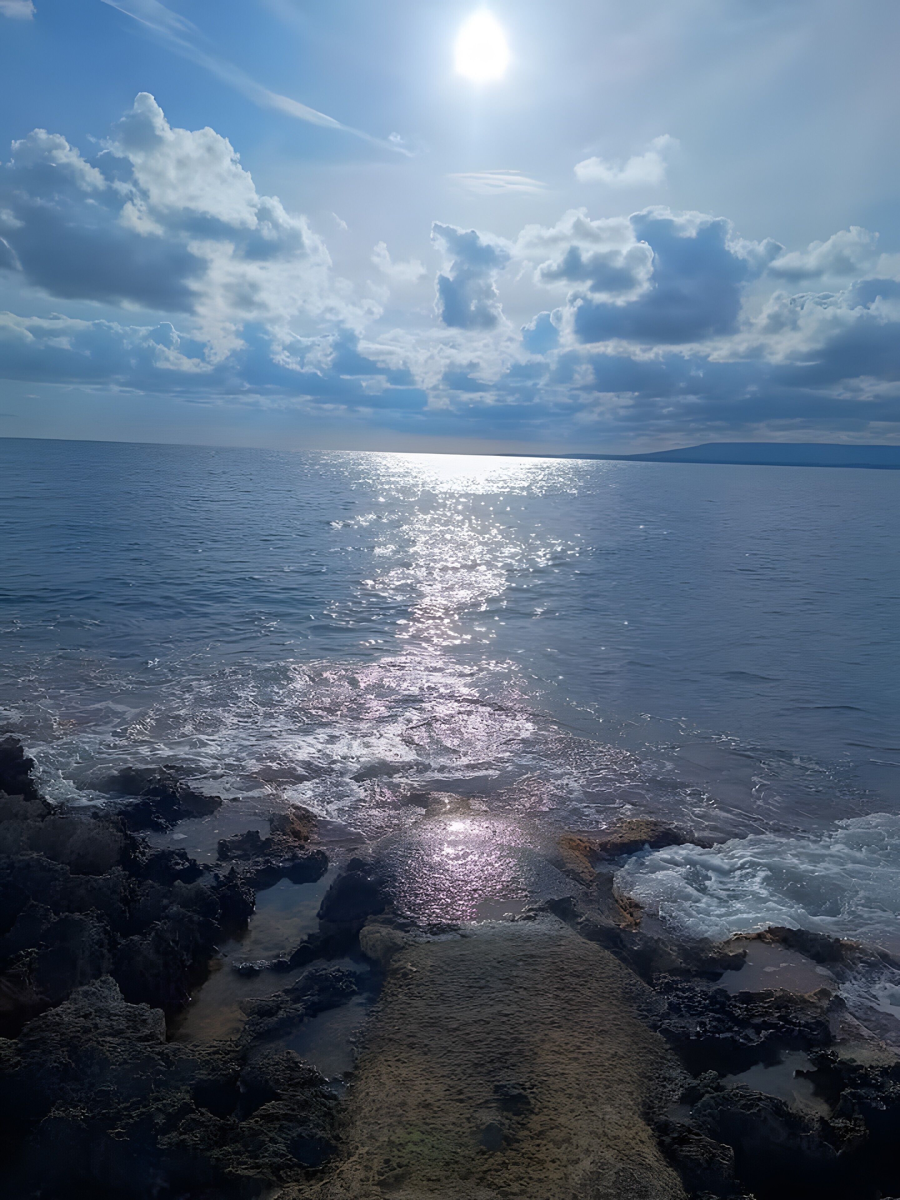 A coastal view with a rocky shoreline, calm sea, and a clear sky.