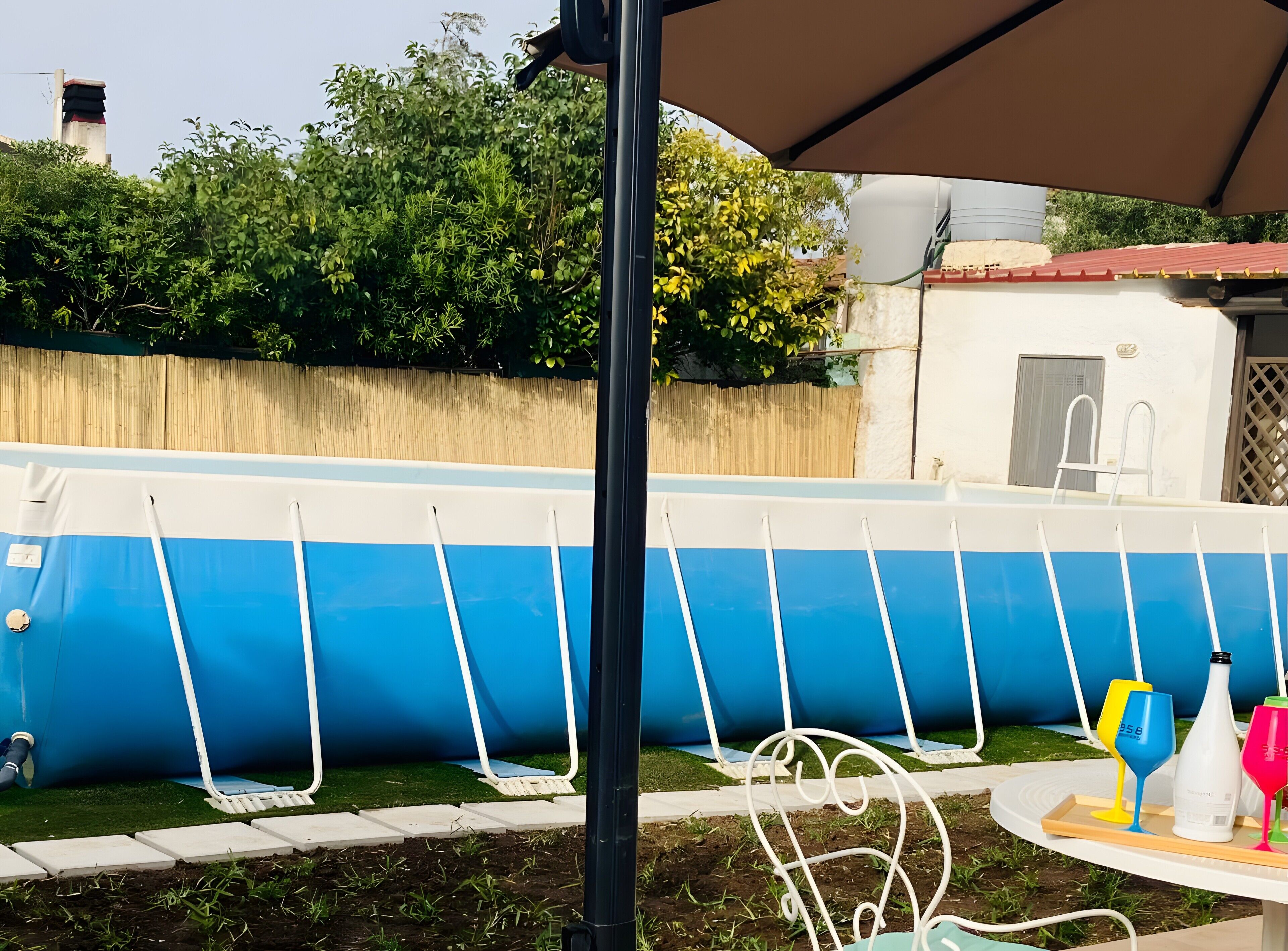 A swimming pool with a blue and white color scheme, surrounded by a wooden fence and greenery.