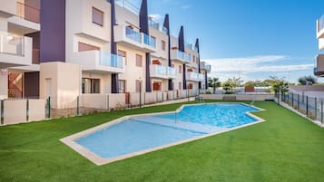 A modern apartment building with a swimming pool and green lawn.