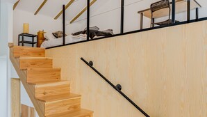 A wooden staircase with a metal handrail, a bed with pillows, a small table with a lamp, and a chair on a platform. - Apartment 'Azores4fun' with Wi-Fi & AC (Horta)