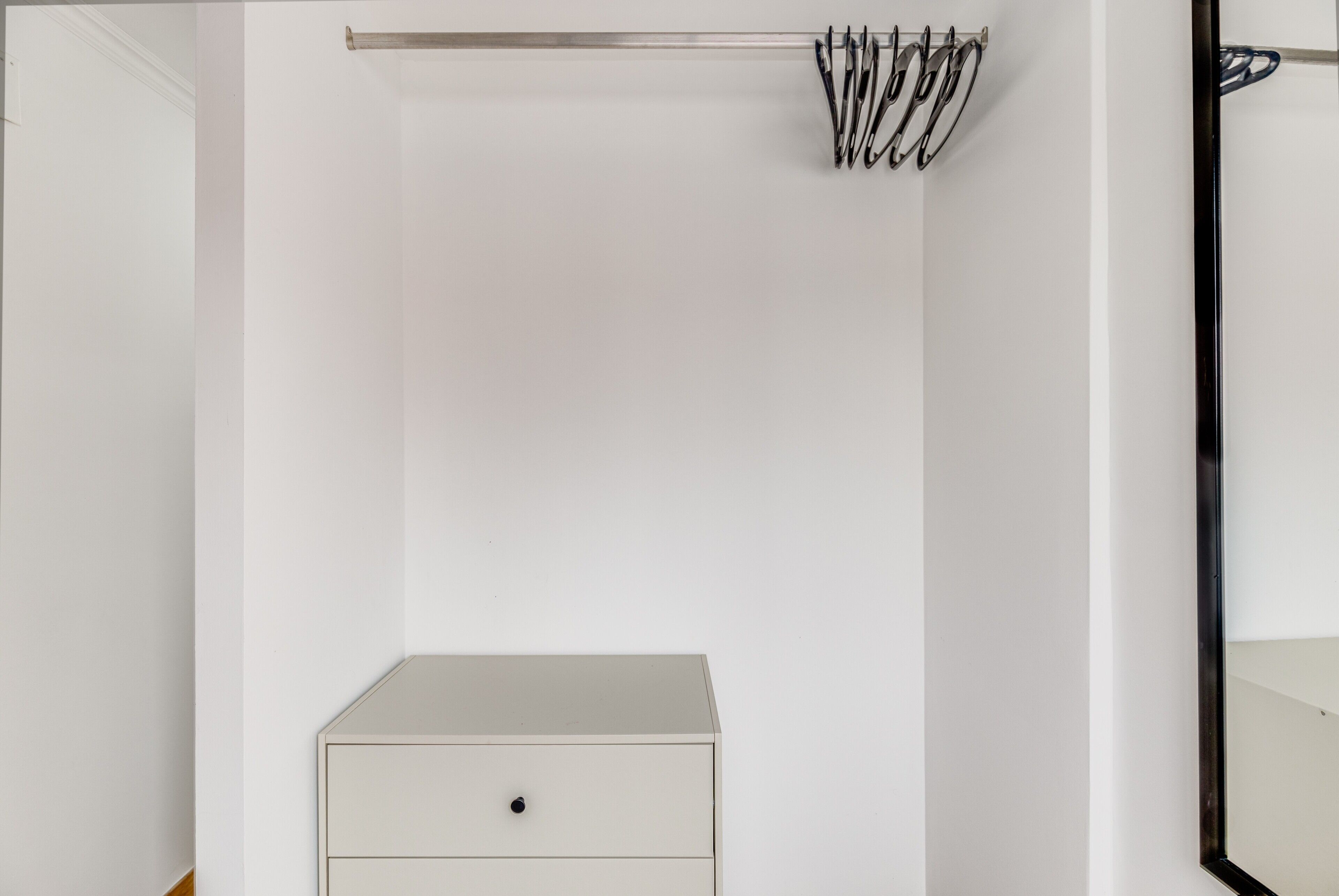 Une armoire blanche avec une tringle en métal et des crochets fixés au-dessus.