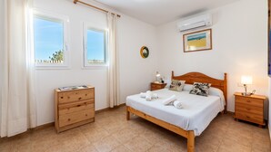 Une chambre à coucher avec un lit, une commode en bois, des tables de chevet et une fenêtre avec des rideaux.