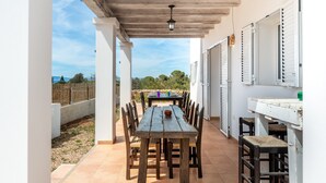 Une terrasse extérieure avec une table et des chaises en bois, un luminaire suspendu et une vue sur le paysage environnant.