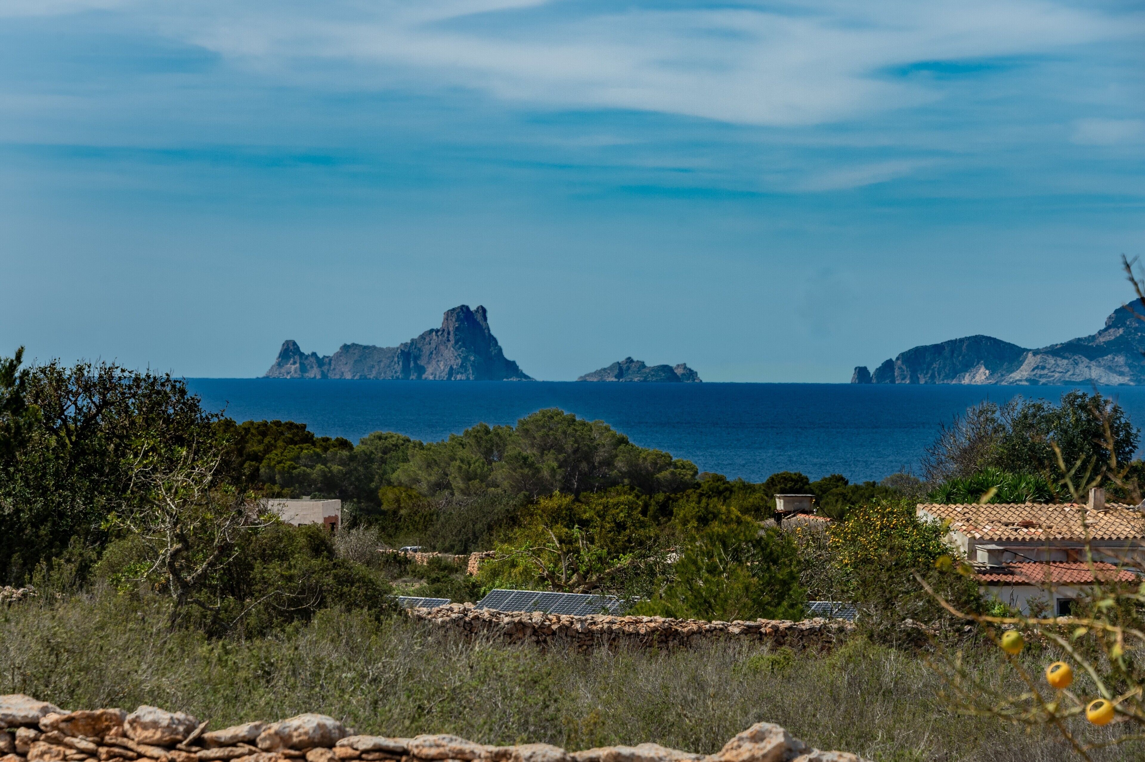 A coastal landscape with rocky outcrops, a clear sky, and a view of the sea.