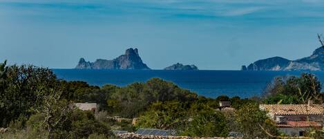 A coastal landscape with rocky outcrops, a clear sky, and a view of the sea.