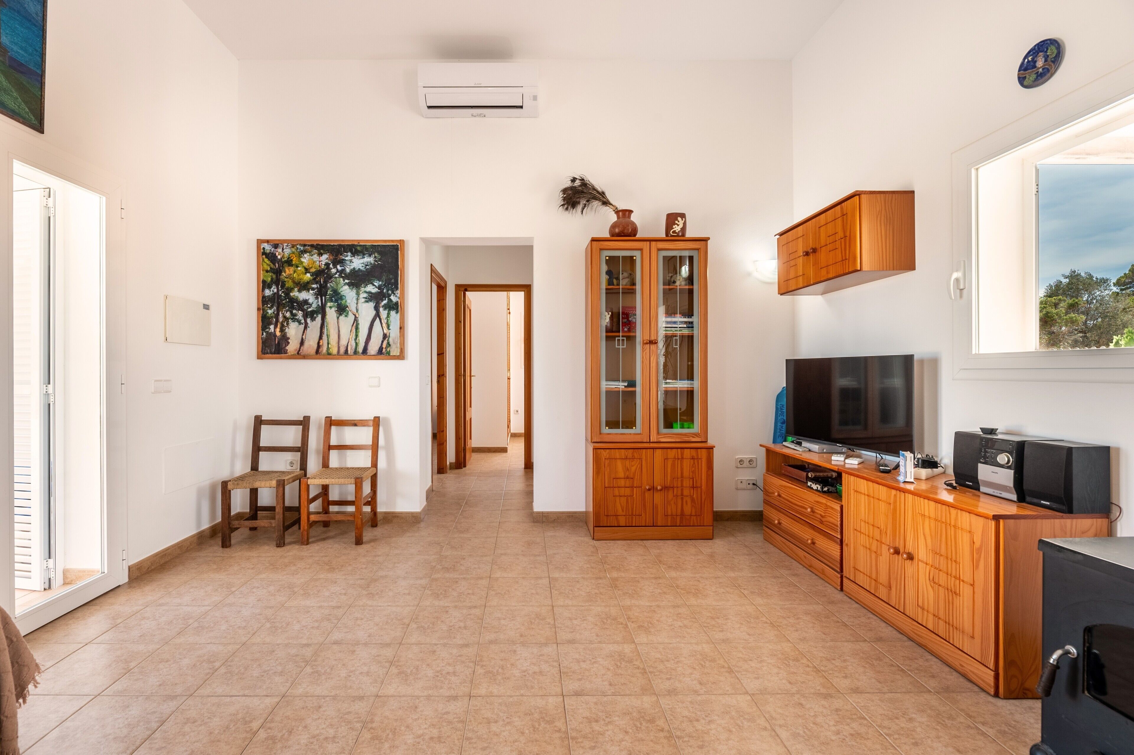 Quarto com televisão, armários de madeira, um quadro e porta que dá para outro cômodo.
