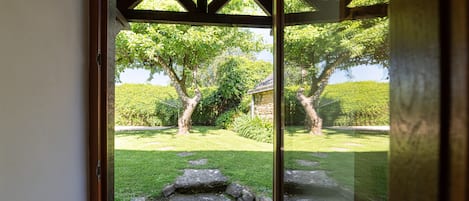 A view through a glass door with a stone pathway leading to a grassy area with trees and a stone building.