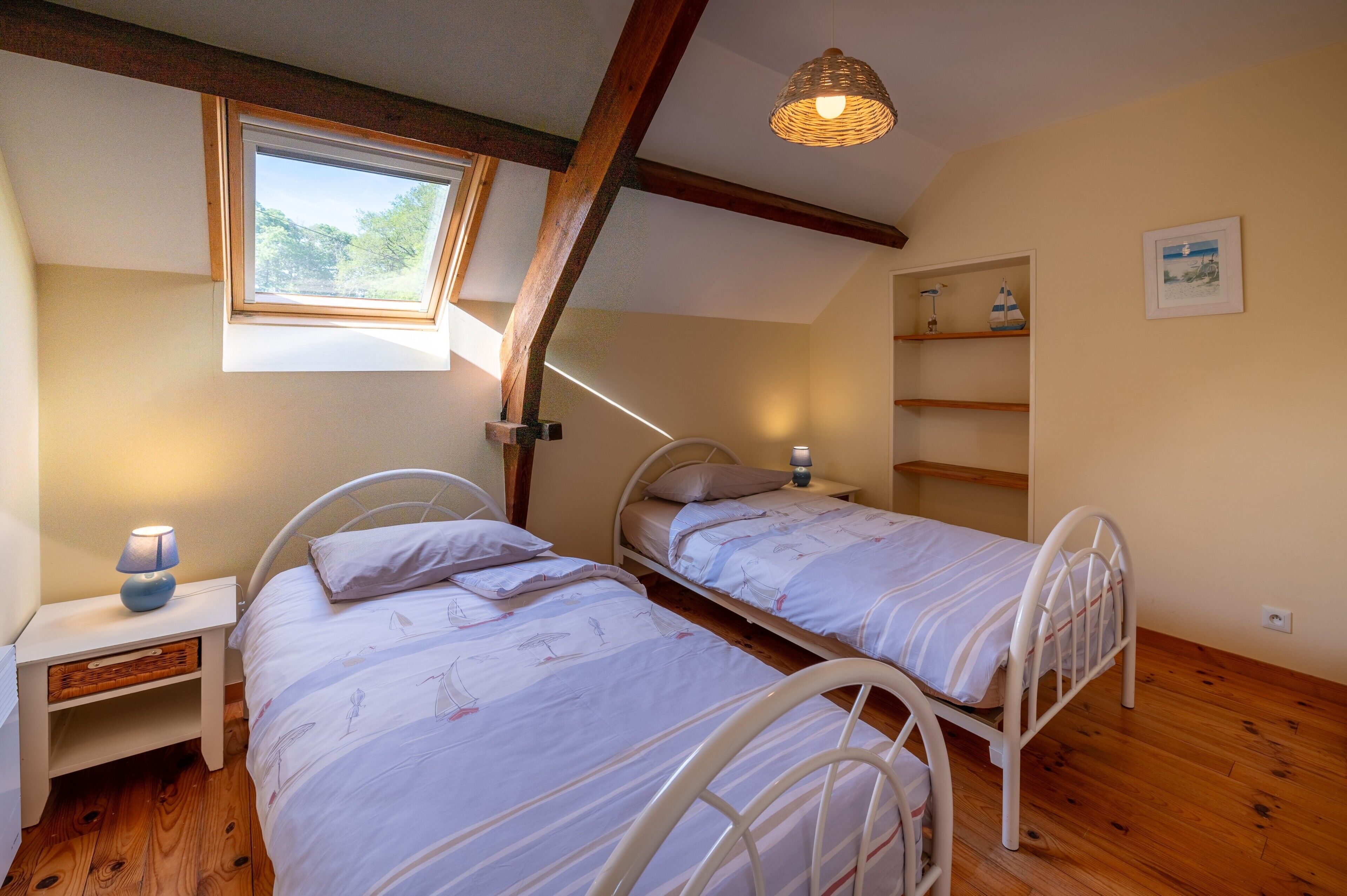 Une chambre avec deux lits, une lucarne, une lampe de chevet et une étagère ornée d’objets décoratifs.