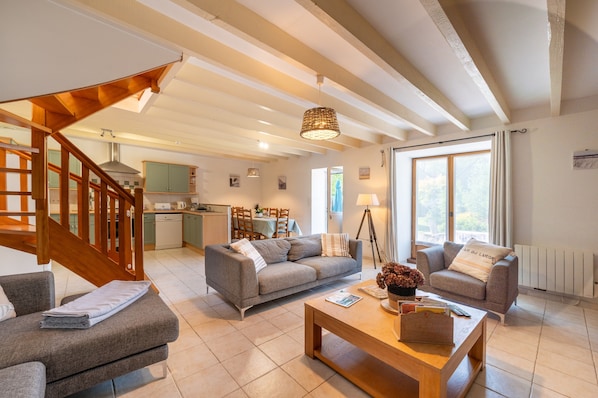 A spacious living area with a staircase, two sofas, a coffee table, and a dining area in the background.