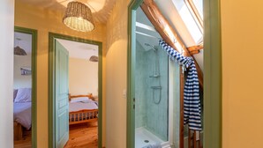 Une pièce avec un plancher en bois, un lit, une porte verte, une douche avec une porte en verre et un luminaire suspendu.