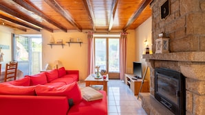 Un salon avec un canapé rouge, une cheminée, un téléviseur et un mur en pierre.