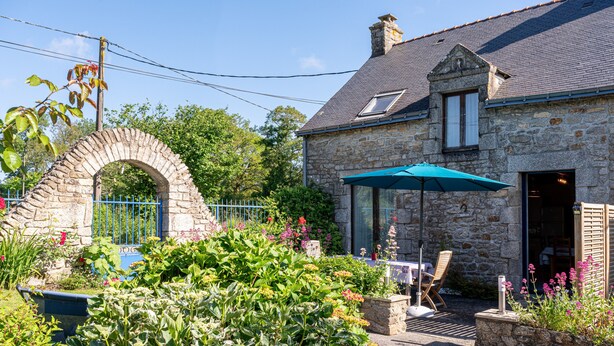 Un bâtiment en pierre doté d’un patio, d’une table avec des chaises et d’un parasol bleu.
