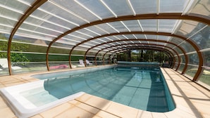 Une piscine intérieure couverte, dotée d’un toit en verre et offrant une vue sur l’extérieur.