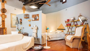 Una habitación de hotel acogedora con una cama, una silla de mimbre, una mesita pequeña y una estantería.