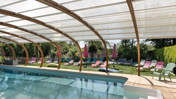 Una piscina con un recinto in vetro, sedie a sdraio e ombrelloni.