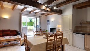 Zona pranzo con tavolo e sedie, un divano, una televisione e angolo cottura con lavastoviglie.