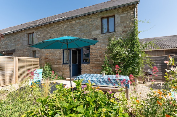 A stone house with a patio, a table with a tablecloth, and a green umbrella.