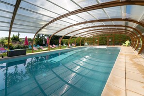 A covered swimming pool with lounge chairs and umbrellas.