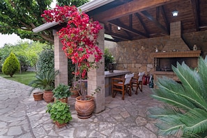 A stone patio with potted plants, a wooden table and chairs, and a stone fireplace.
