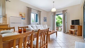 A dining area with a wooden table and chairs, a sofa, a television, and a view of greenery through the open door. - Apartment 'Villa Rita' with Shared Garden, Wi-Fi and Air Conditioning (?e???da)