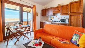 A compact living space with a dining area, a sofa, a kitchen, and a sliding glass door to a balcony. - Apartment 'Bella Vista Castelsardo' with Sea View, Balcony and Air Conditioning (Castelsardo)