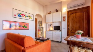 A living room with a sofa, a TV, a wooden door, and a cabinet with a TV on top. - Apartment 'Bella Vista Castelsardo' with Sea View, Balcony and Air Conditioning (Castelsardo)