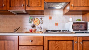 A kitchen with wooden cabinets, a microwave, a stove, and various kitchen utensils. - Apartment 'Bella Vista Castelsardo' with Sea View, Balcony and Air Conditioning (Castelsardo)