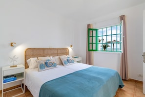 A room with a bed, a nightstand, a window with curtains, and a view of palm trees outside. -  'Alma Ocean View' with Sea View, Shared Pool and Wi-Fi (Puerto del Carmen)
