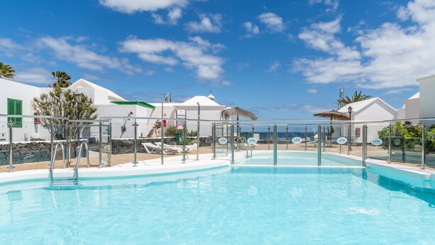 A swimming pool with a clear blue sky, white buildings, and lounge chairs. -  'Alma Ocean View' with Sea View, Shared Pool and Wi-Fi (Puerto del Carmen)