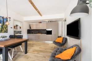 A modern kitchen with a TV, dining area with a table and chairs, and a living area with a sofa and TV.