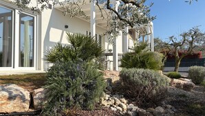 Un bâtiment moderne doté de grandes fenêtres, d’un espace extérieur couvert et d’un jardin aménagé avec des rochers et des arbustes.